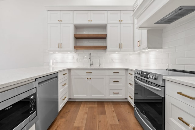 kitchen featuring light wood-style flooring, custom range hood, a sink, stainless steel appliances, and white cabinetry