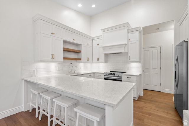 kitchen with a sink, appliances with stainless steel finishes, light wood-type flooring, and a peninsula