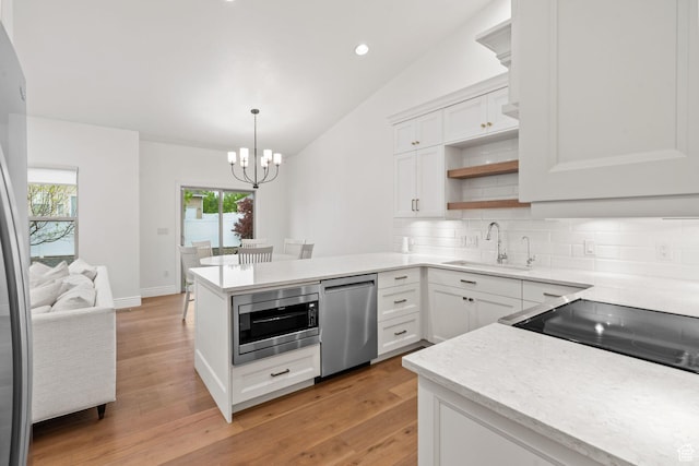 kitchen featuring a peninsula, lofted ceiling, a chandelier, a sink, and stainless steel appliances