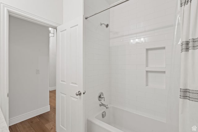 bathroom featuring baseboards, wood finished floors, and shower / bath combo