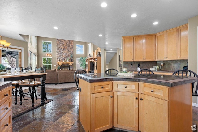 288 S Hillside Dr E, Elk Ridge, UT 84651 - kitchen featuring stone tile flooring, light brown cabinetry, dark countertops, a stone fireplace, and tasteful backsplash