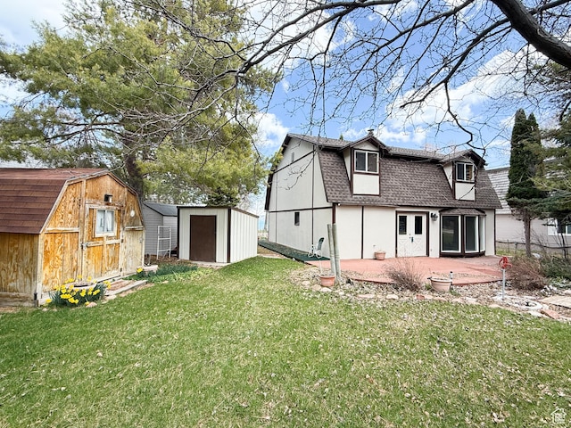 back of property with a patio, a gambrel roof, a shingled roof, a lawn, and a storage shed