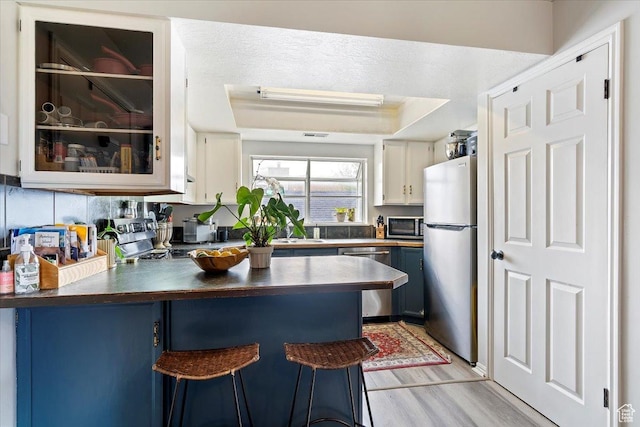 kitchen with a peninsula, dark countertops, light wood-style floors, blue cabinets, and stainless steel appliances