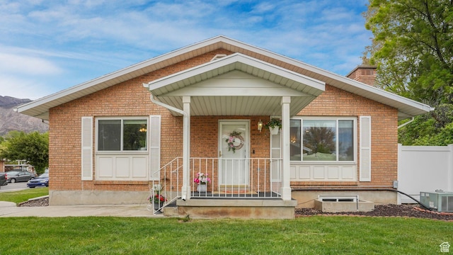 bungalow-style home with central AC unit, a chimney, a front yard, and brick siding