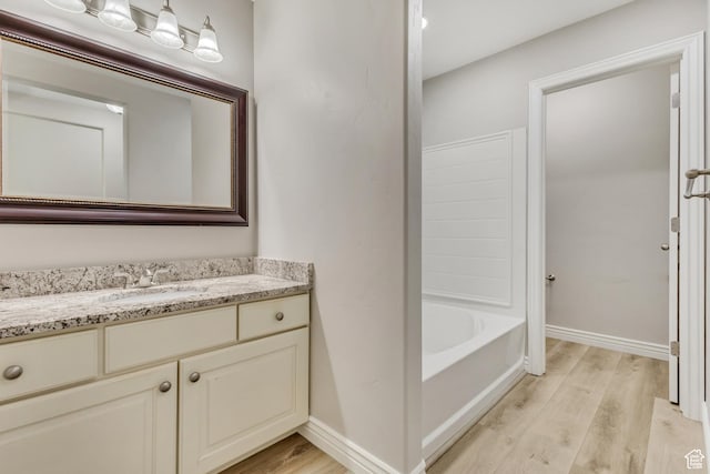 full bathroom featuring vanity, baseboards, wood finished floors, and a tub