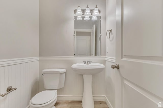 half bathroom featuring toilet, wainscoting, and a sink