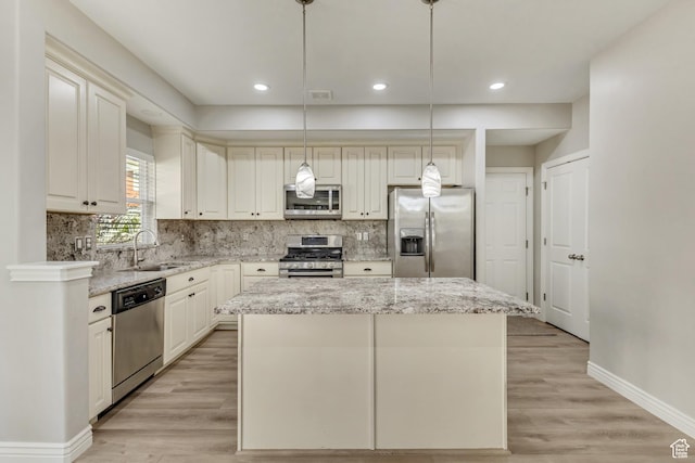 kitchen with light stone countertops, appliances with stainless steel finishes, a sink, a center island, and baseboards