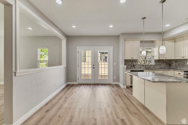 kitchen featuring light stone counters, light wood-style floors, french doors, decorative light fixtures, and decorative backsplash