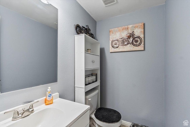 bathroom featuring vanity, a textured wall, toilet, and visible vents