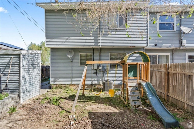 rear view of house featuring fence, central air condition unit, and a playground