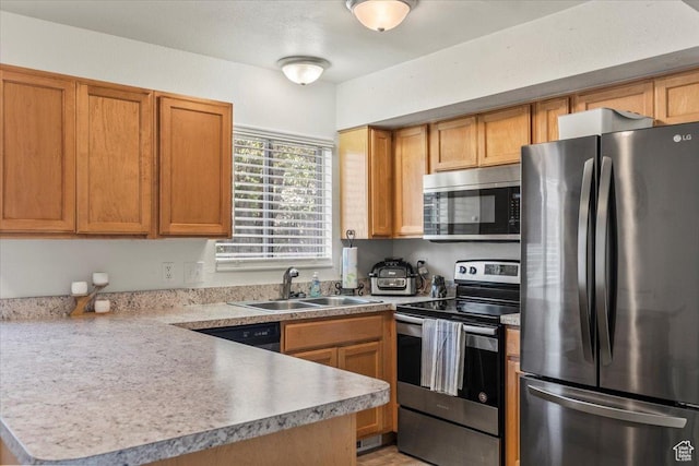 kitchen with light countertops, a peninsula, appliances with stainless steel finishes, and a sink