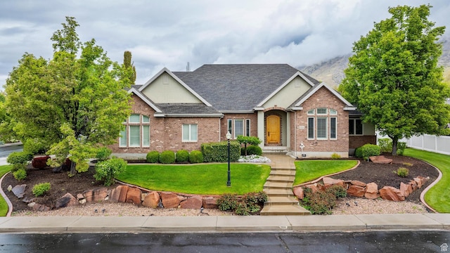 view of front of home with brick siding, a front lawn, roof with shingles, and fence