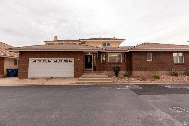 prairie-style home with brick siding, an attached garage, and a chimney