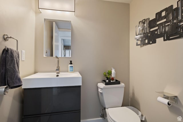half bathroom with vanity, baseboards, and toilet