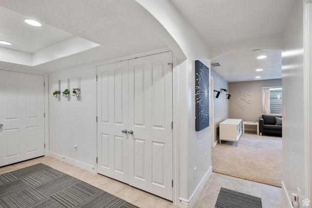 interior space with light colored carpet, a raised ceiling, arched walkways, recessed lighting, and baseboards