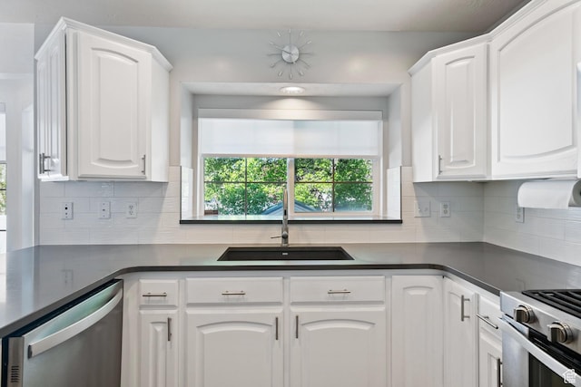 kitchen featuring white cabinets, dark countertops, a sink, stainless steel appliances, and tasteful backsplash
