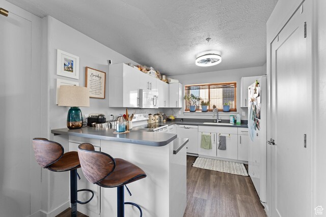 1700 S Sandhill Rd S Unit F301, Orem, UT 84058 - kitchen with white cabinets, a sink, white appliances, a peninsula, and dark wood-style floors