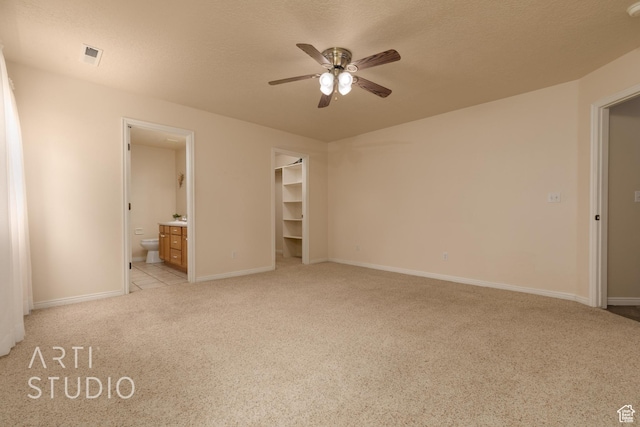 unfurnished bedroom with a walk in closet, visible vents, light colored carpet, baseboards, and ensuite bathroom