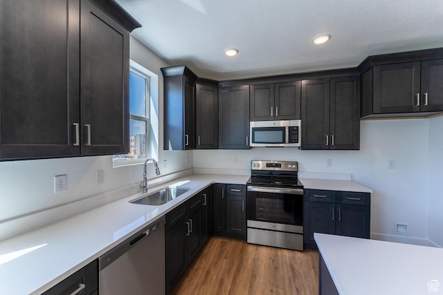 kitchen featuring appliances with stainless steel finishes, wood finished floors, a sink, light countertops, and recessed lighting