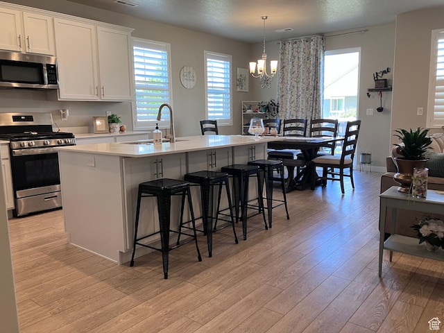 1831 S 2525 W Unit 103, West Haven, UT 84401 - kitchen featuring stainless steel appliances, light wood-style floors, a center island with sink, a kitchen bar, and light countertops