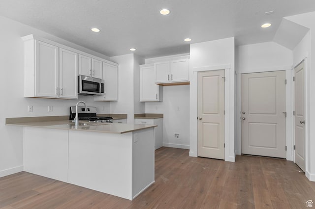 kitchen with a peninsula, baseboards, recessed lighting, white cabinets, and appliances with stainless steel finishes