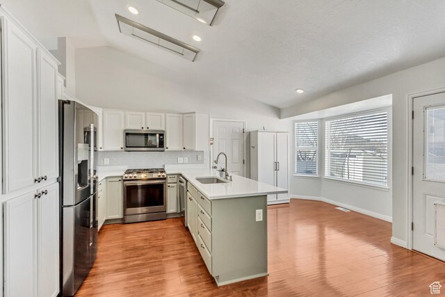 5943 N Genoa Ln W, Stansbury Park, UT 84074 - kitchen featuring appliances with stainless steel finishes, a sink, light wood finished floors, backsplash, and vaulted ceiling