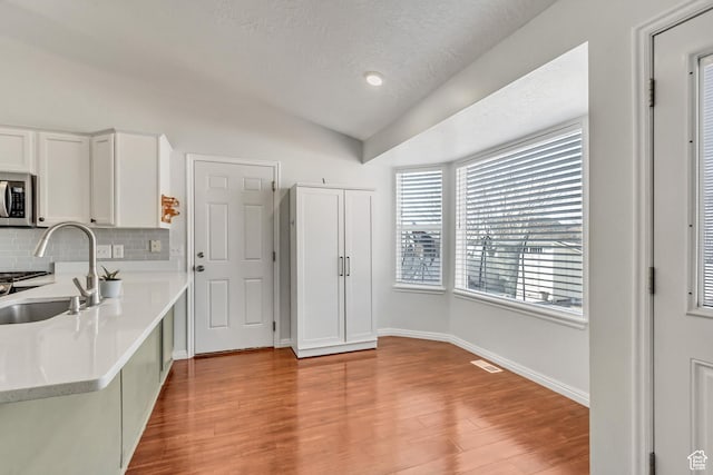 5943 N Genoa Ln W, Stansbury Park, UT 84074 - kitchen featuring lofted ceiling, light countertops, stainless steel microwave, a sink, and backsplash