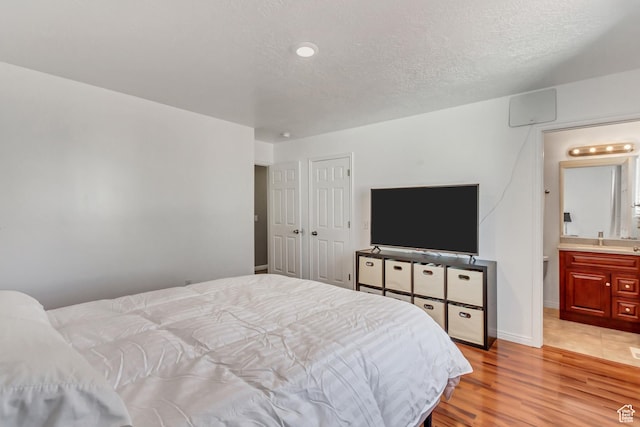 5943 N Genoa Ln W, Stansbury Park, UT 84074 - bedroom featuring connected bathroom, a textured ceiling, baseboards, and light wood-style floors
