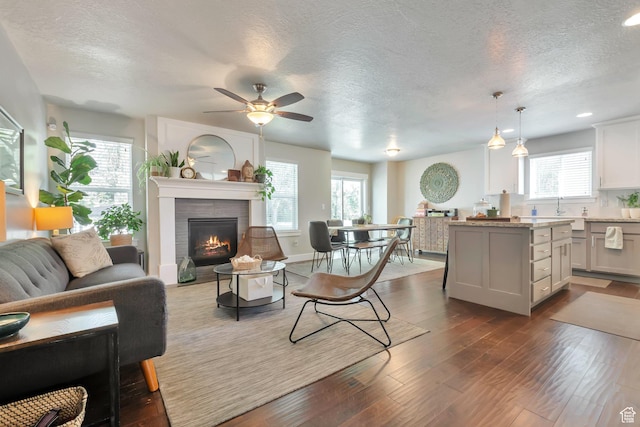 494 N 300 E, American Fork, UT 84003 - living room with a ceiling fan, a textured ceiling, dark wood-style flooring, and a warm lit fireplace