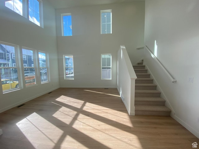 unfurnished living room featuring stairway, baseboards, wood finished floors, and a towering ceiling