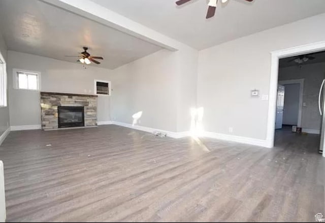 unfurnished living room with baseboards, a stone fireplace, a ceiling fan, and wood finished floors