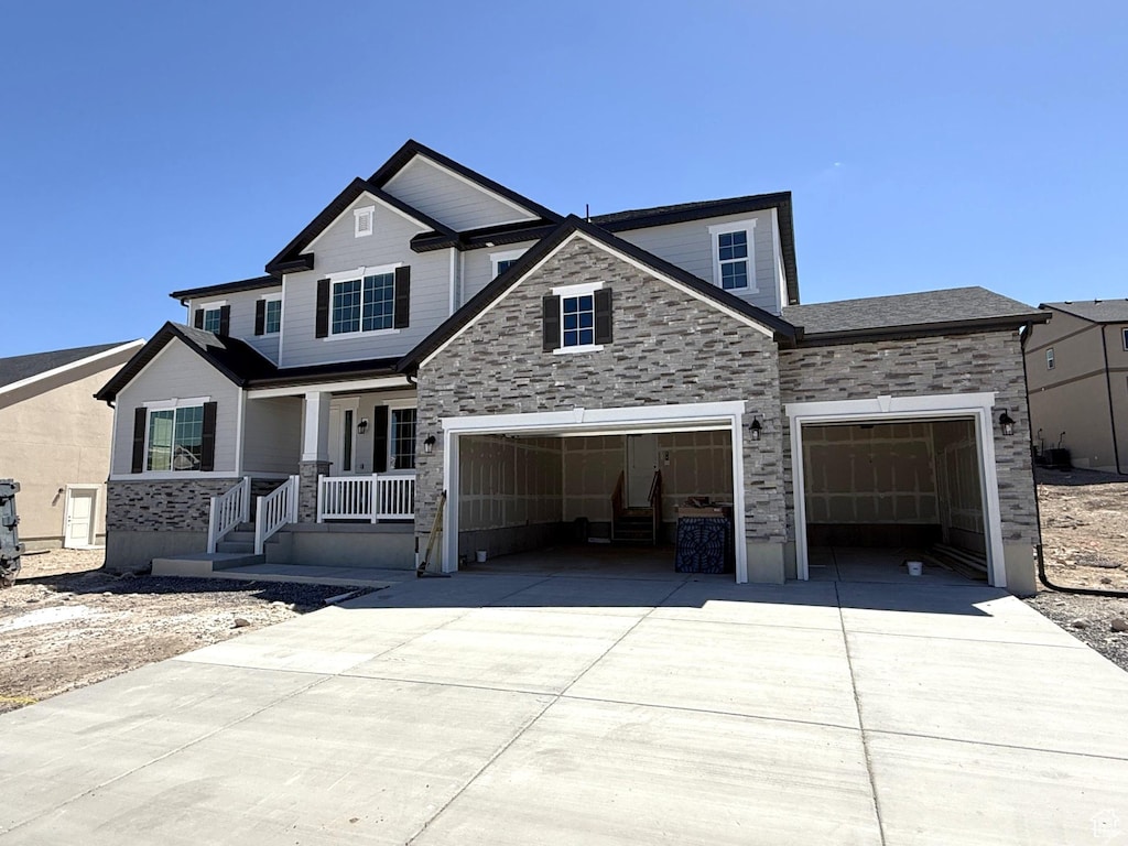 craftsman inspired home with covered porch, an attached garage, stone siding, and driveway