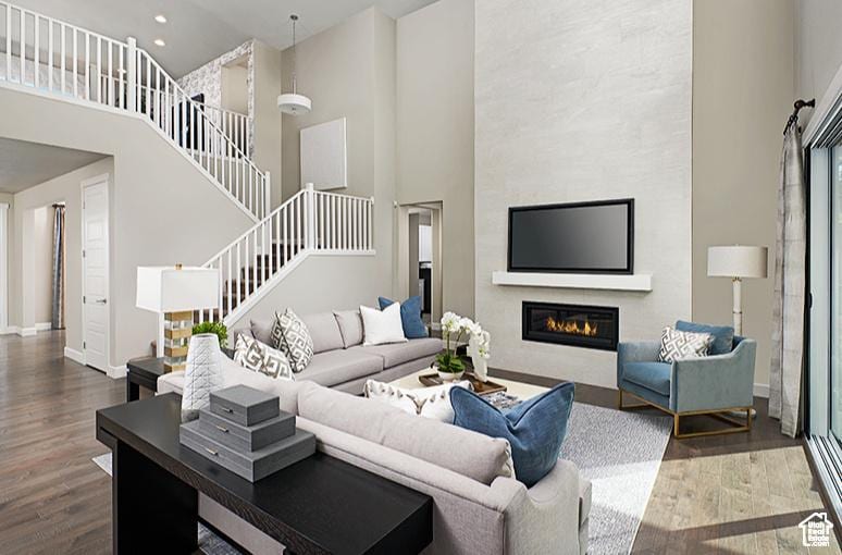 living room featuring stairway, wood finished floors, a high ceiling, and a glass covered fireplace
