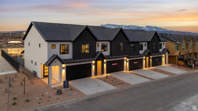 view of front facade featuring driveway, fence, a mountain view, an attached garage, and stucco siding