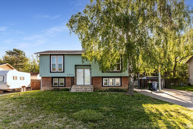raised ranch with board and batten siding, brick siding, fence, and a front yard