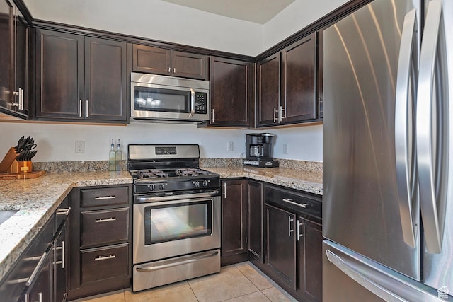 kitchen with dark brown cabinetry, light tile patterned flooring, light stone countertops, and stainless steel appliances