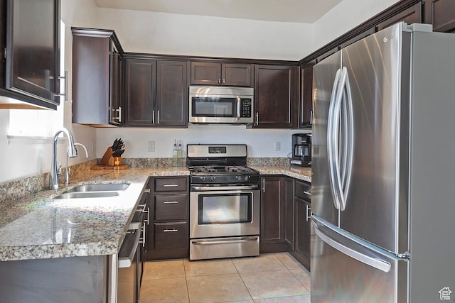 kitchen with dark brown cabinetry, appliances with stainless steel finishes, light stone countertops, a sink, and light tile patterned flooring