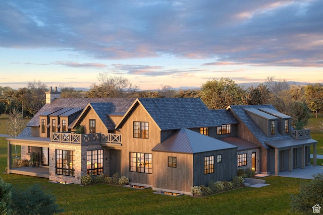 back of house at dusk featuring a standing seam roof, a yard, metal roof, and a balcony