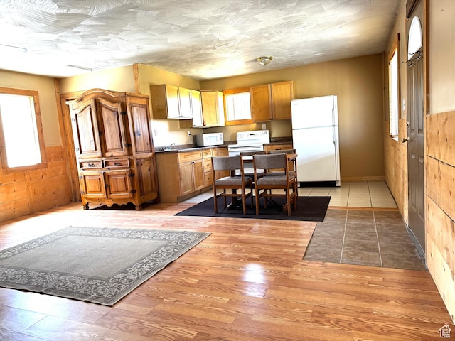 848 N Cooley St W, Grantsville, UT 84029 - kitchen with brown cabinetry, dark countertops, a wainscoted wall, white appliances, and light wood-style flooring