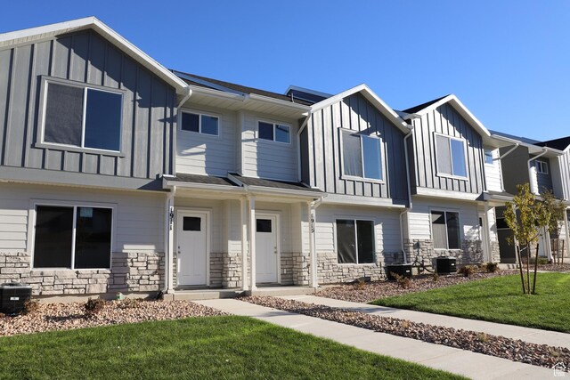 view of property with board and batten siding, cooling unit, stone siding, and a front lawn