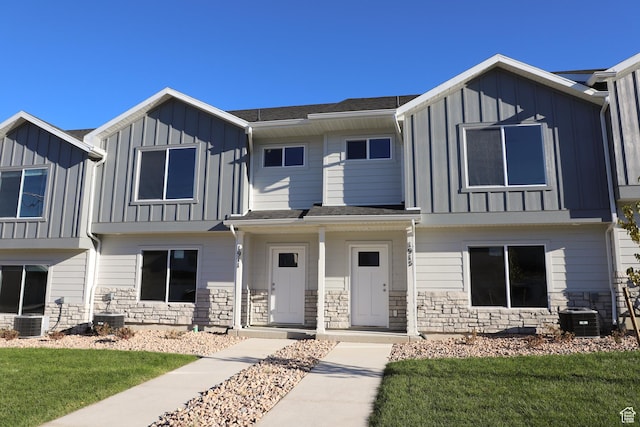 townhome / multi-family property with board and batten siding, a front yard, stone siding, and central air condition unit