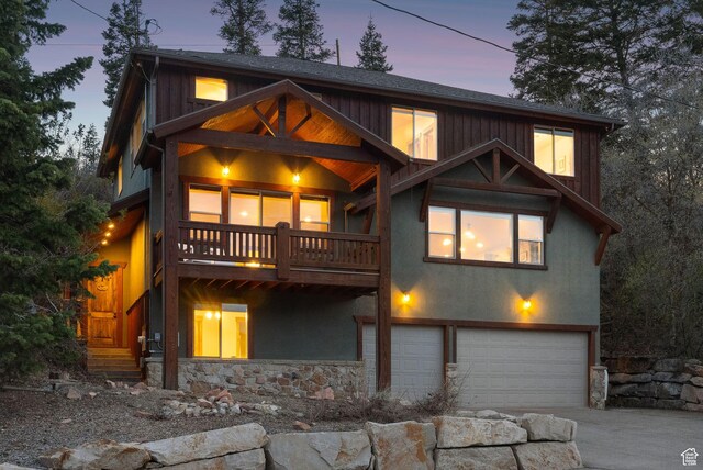 210 Parkview Dr, Summit Park, UT 84098 - back of house at dusk with a garage, a balcony, stone siding, stucco siding, and concrete driveway