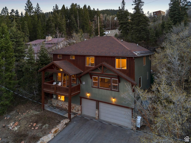 chalet / cabin featuring roof with shingles, an attached garage, stone siding, a forest view, and driveway