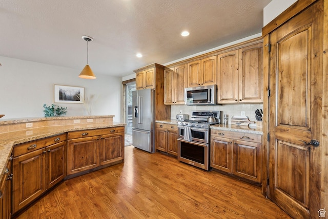 210 Parkview Dr, Summit Park, UT 84098 - kitchen featuring brown cabinetry, wood finished floors, light stone countertops, appliances with stainless steel finishes, and decorative light fixtures