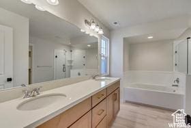 full bathroom featuring a garden tub, double vanity, wood finished floors, a sink, and a stall shower