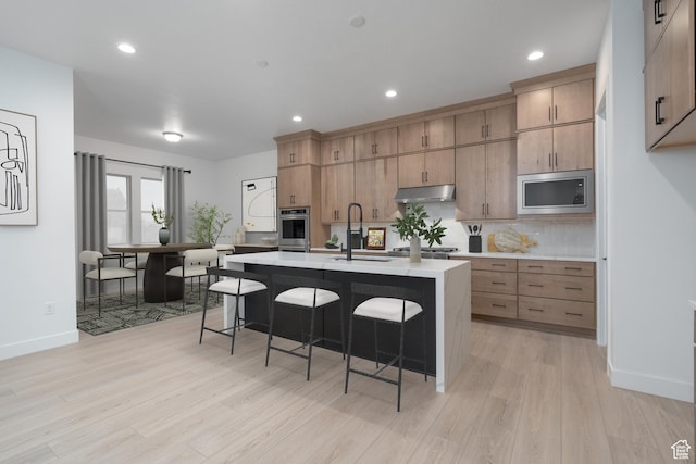 kitchen featuring a breakfast bar, a sink, light wood-style flooring, stainless steel appliances, and under cabinet range hood