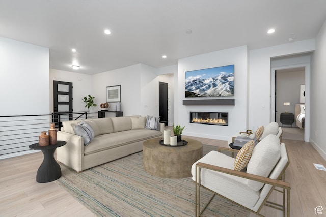 living room with light wood-style floors, baseboards, a glass covered fireplace, and recessed lighting