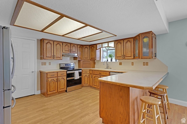 2137 W 550 N, West Point, UT 84015 - kitchen featuring appliances with stainless steel finishes, brown cabinetry, a peninsula, light wood-type flooring, and under cabinet range hood
