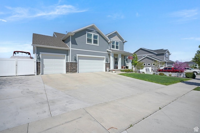 view of front of property with fence, a front lawn, stone siding, a gate, and driveway