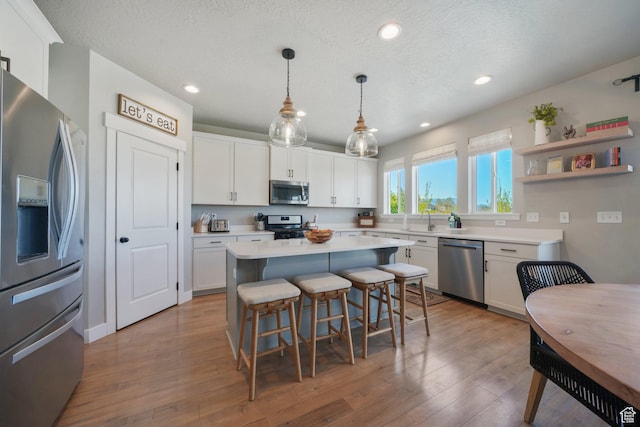 kitchen featuring a kitchen breakfast bar, a sink, light countertops, white cabinets, and stainless steel appliances
